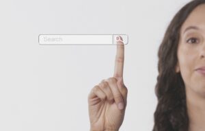 A finger points to the magnifying glass icon within a search bar on a plain white background.